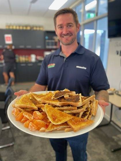 An individual wearing a blue Komatsu and Live Your Dream polo, smiling and holding a large plate of assorted foods.