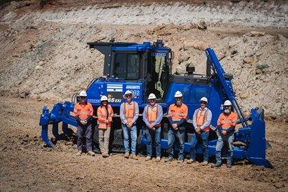 Group of workers in safety gear standing in front of a large blue Komatsu bulldozer at a construction site.