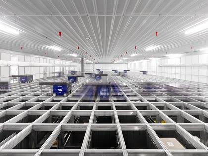 Interior of a fulfillment center with packages and conveyor systems visible under a vast, brightly lit ceiling.