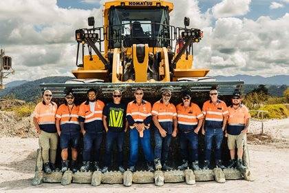 Group of construction workers in safety gear standing in front of a Komatsu loader.
