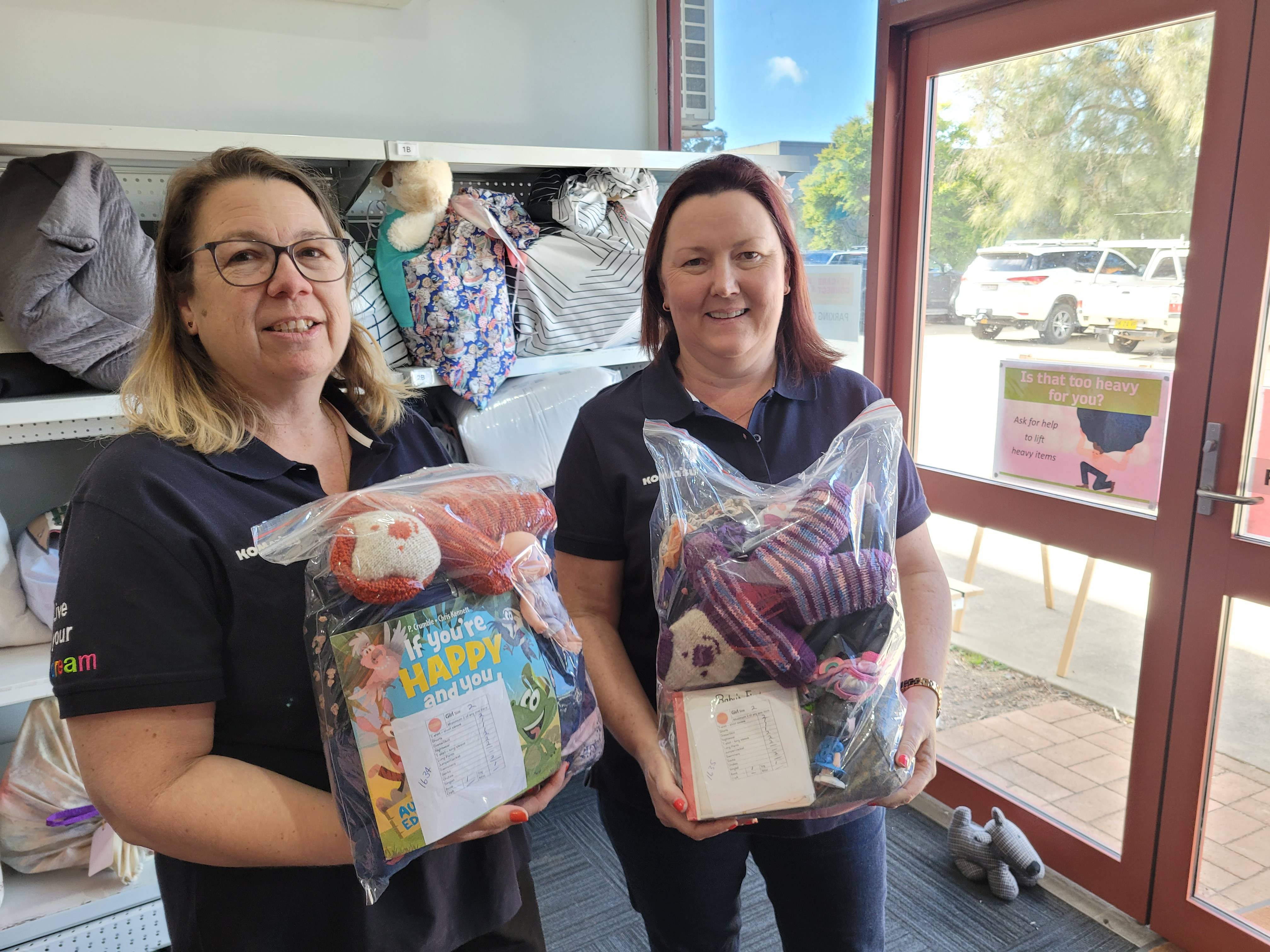 Two volunteers, each holding a bag of donated items, smiling at the camera.