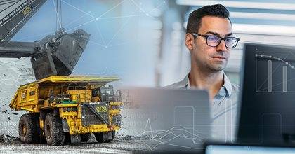 Professional using a laptop with a backdrop of a large mining truck and industrial graphics.