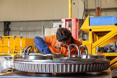 Worker in high visibility uniform working on large machine part in workshop.