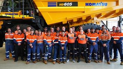 Group of workers in high visibility clothing standing in front of a Komatsu HD605 truck.