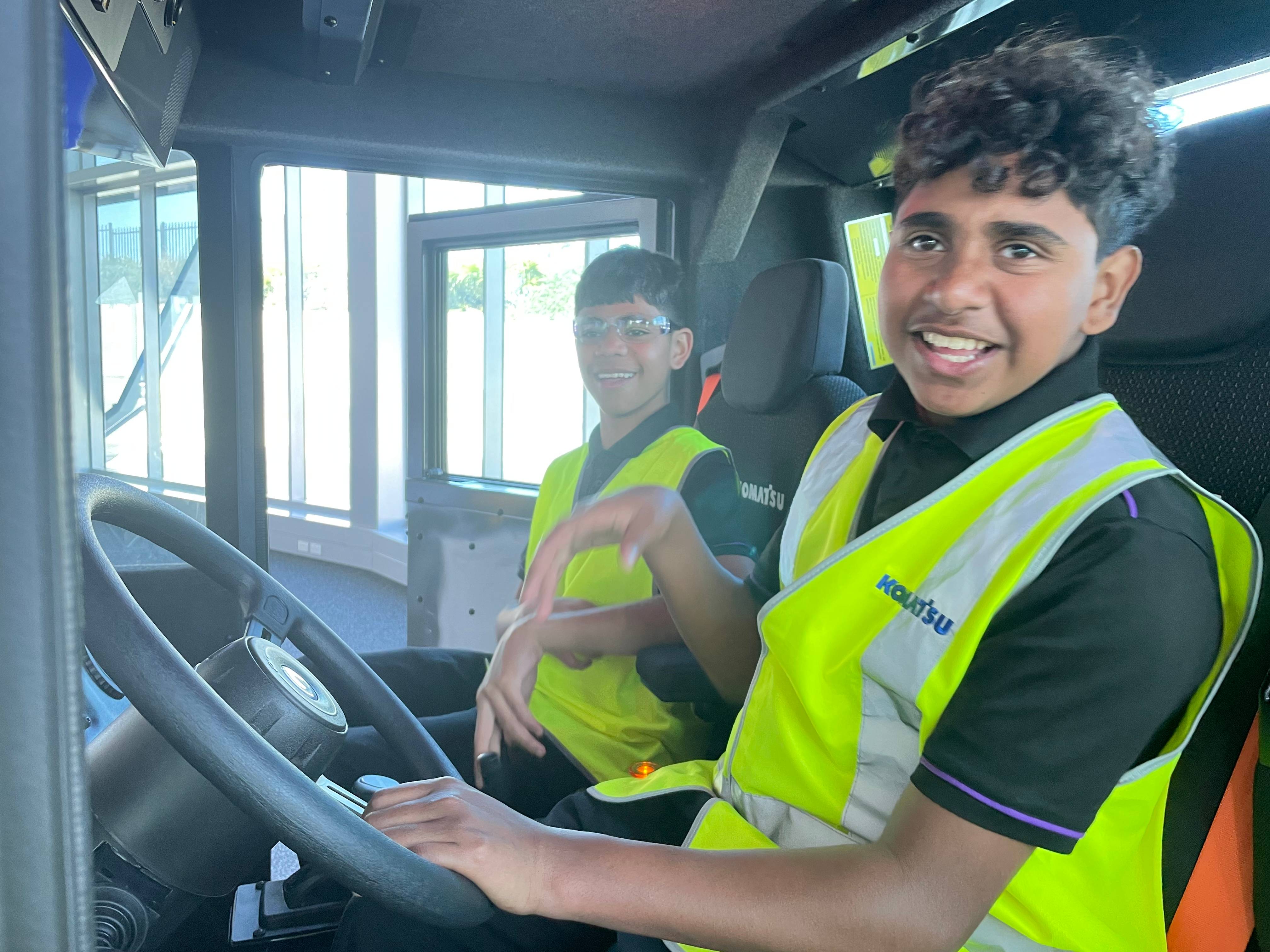 Two boys wearing hi vis vests sitting inside machine cab