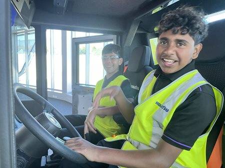 Two boys wearing hi vis vests sitting inside machine cab