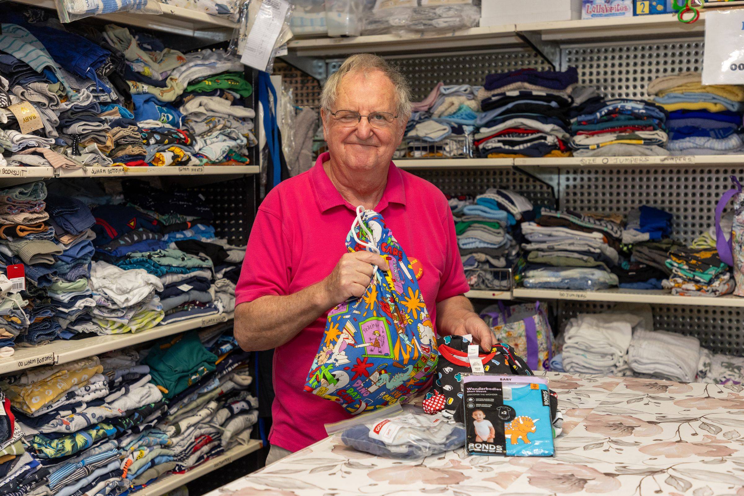 A man smiling, standing behind a counter with various baby products including clothing and toys.