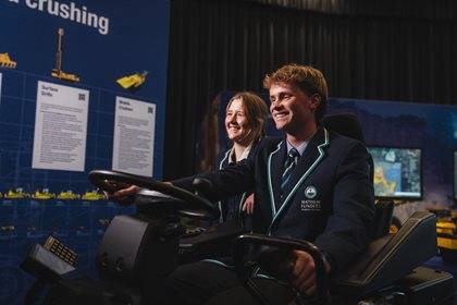 Two students in uniforms interact with a simulation exhibit, smiling as they operate the equipment