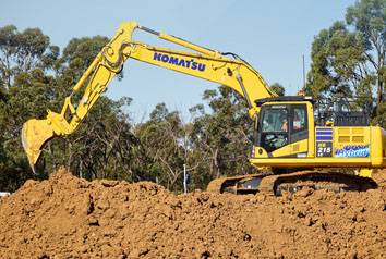 A yellow Komatsu excavator sitting on top of a dirt pile with its arm extended.