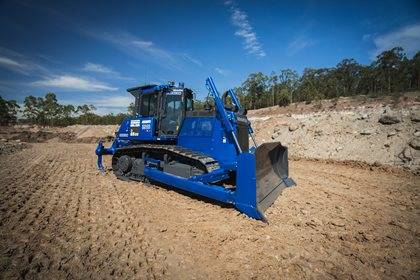 A Komatsu bulldozer on a bare dirt terrain under a clear sky.