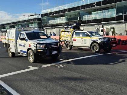 Two Komatsu service vehicles parked on a racetrack, with bright sunlight and clear skies.