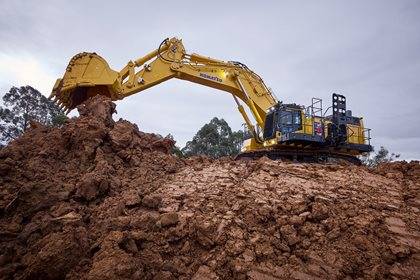 A large yellow Komatsu excavator working on a pile of orange dirt.