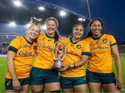 Four rugby players in Australian jerseys smiling and holding a trophy at a stadium.
