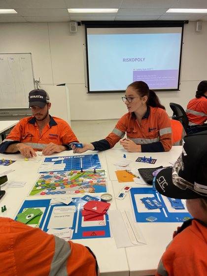 Two individuals in high-visibility orange workwear are seated at a table playing a board game.
