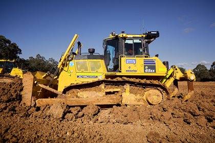 A Komatsu D65EX bulldozer operates on a dirt field.