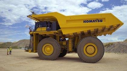 Two workers stand near a large Komatsu dump truck at a mining site under a cloudy sky.
