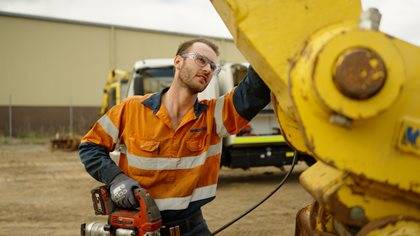 A heavy diesel mechanic wearing hi vis uniform inspecting a Komatsu machine on a worksite.
