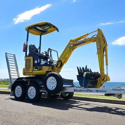 A yellow Komatsu excavator on a trailer under a blue sky with water views in the background.
